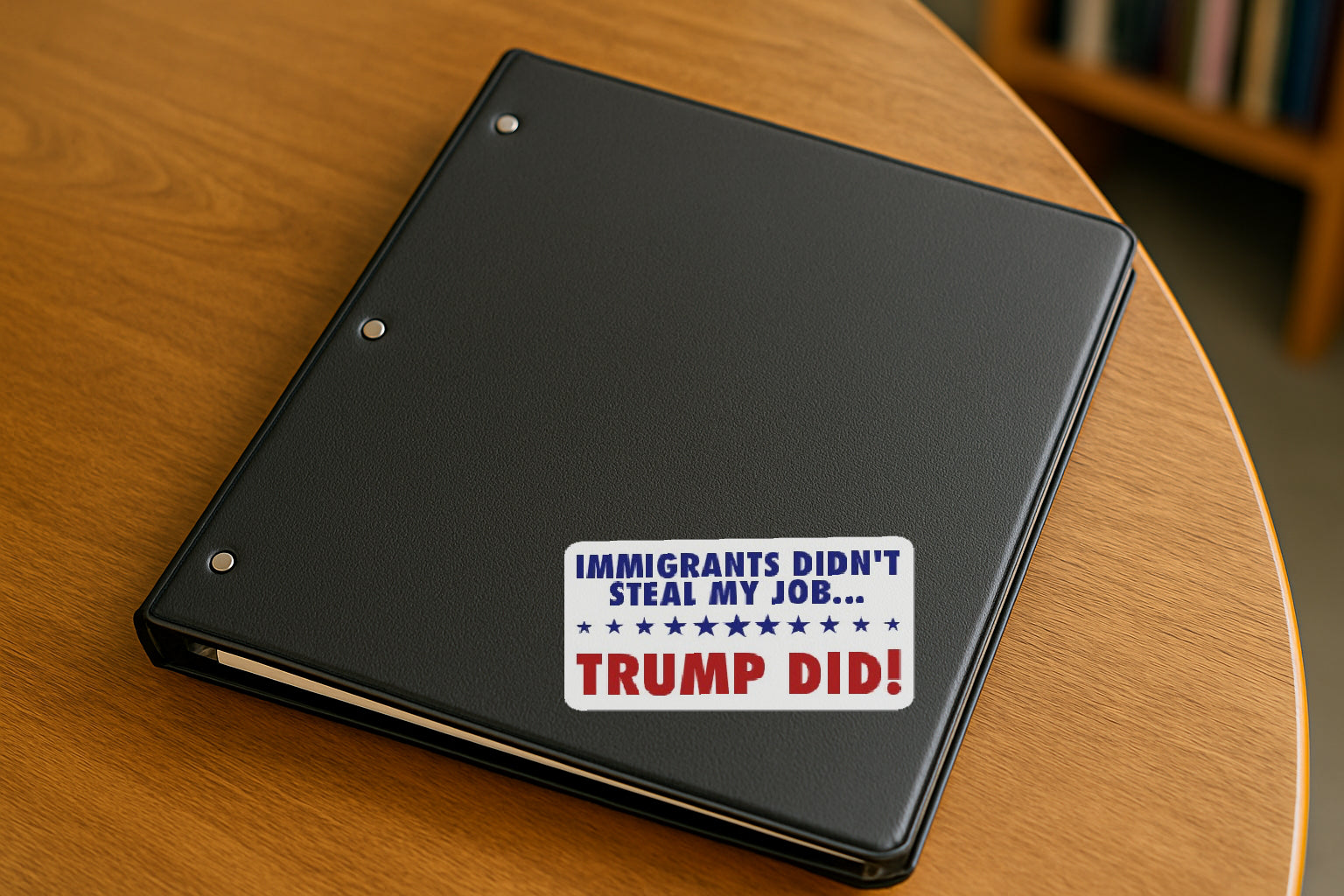 Immigrants Didn't Steal My Job  Trump Did' magnet or vinyl decal displayed on a black binder in a library. A bold, high-quality political sticker perfect for cars, laptops, fridges, or toolboxes. Great for activists, protestors, or anyone fed up with fascism.
