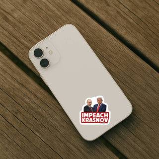 An overhead shot of the sticker placed on the back of an off-white or silver iPhone. The phone is resting diagonally on a weathered wooden surface, like a deck or park bench.