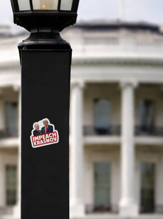 The sticker is stuck to a black metal lamp post in the foreground. In the background, the White House is visible, architecturally distinct but softly blurred to create depth.