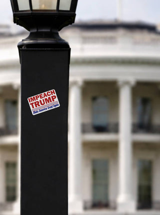 Sticker on a lamp post with 'Impeach Trump' text, blurred background of a building.