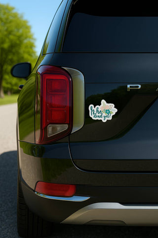 Is he dead yet floral sticker displayed on the rear of a black SUV in daylight