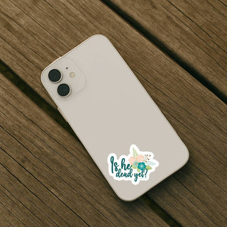 Phone case with 'Is he dead yet?' sticker on a wooden surface