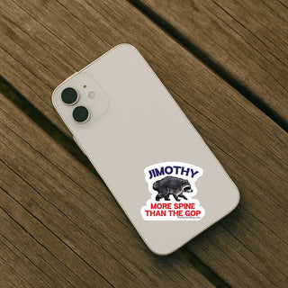 A white smartphone case shown from the back, placed on a brown wooden surface. The case has a die-cut sticker featuring the text 'JIMOTHY' above a black bear and the phrase 'MORE SPINE THAN THE GOP' in red and blue.