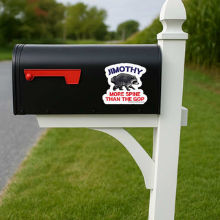 A black mailbox mounted on a white post outdoors, with a white and red sticker that reads 'JIMOTHY MORE SPINE THAN THE GOP' featuring a raccoon graphic.