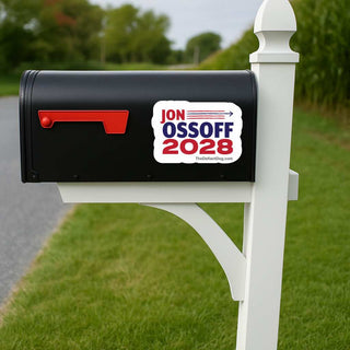 A black mailbox mounted on a white post outdoors, with a white, red, and blue political sticker reading 'JON OSsOFF 2028' on the side.