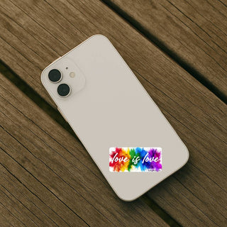 Love is love rainbow paint splash sticker placed on the back of a light colored iPhone resting on a wooden surface