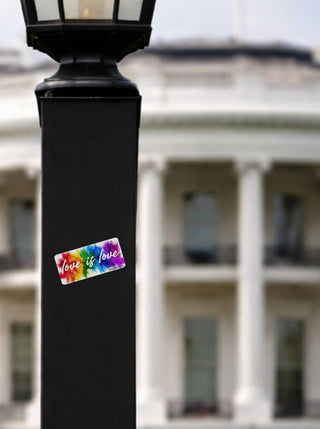Love is love rainbow paint splash sticker on a black lamp post with the White House blurred in the background
