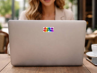Love is love rainbow paint splash sticker centered on the back of a silver laptop at an outdoor café table