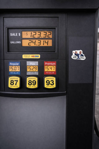 Close-up of a black gas pump display showing sale price, gallons, and three fuel grade buttons labeled 87, 89, and 93. A small sticker with two men is visible on the right side of the pump.