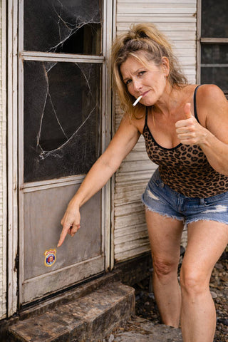 Woman giving a thumbs-up in front of a dilapidated building with a broken window.
