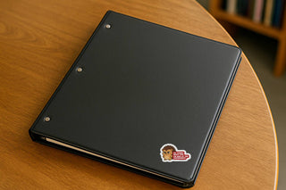 My Tummy Hurts and Im Mad at the Government political humor sticker placed on a black binder resting on a wooden table.