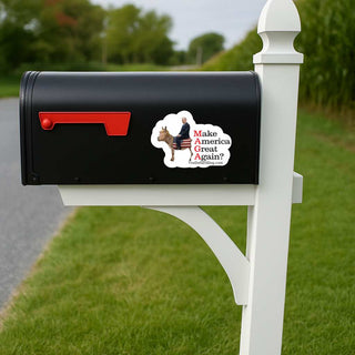 A black mailbox mounted on a white post outdoors, with a red flag and a cloud-shaped sticker that reads 'Make America Great Again?'. A die-cut sticker featuring a trump donkey with an American flag-patterned saddle and netanyahu riding it, alongside the text 'Make America Great Again?' in red and black, and 'TheDefiantDog.com' at the bottom