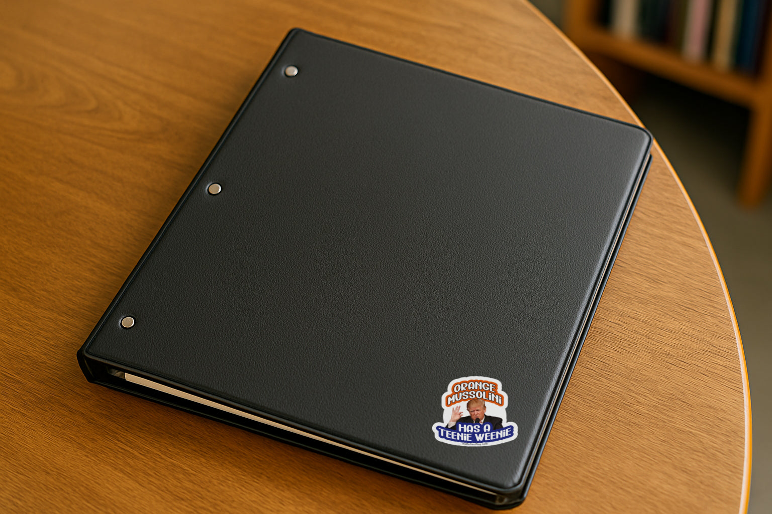 Anti-Trump sticker design featuring “Orange Mussolini Has a Teenie Weenie” with Trump image, available as a weatherproof magnet, vinyl decal, or sticker pack on binder in college library.