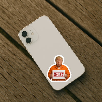 Illustration of Donald Trump in an orange prison jumpsuit holding a sign that reads “8647,” referencing him as the 47th president; image includes TheDefiantDog.com at the bottom on back of iphone.