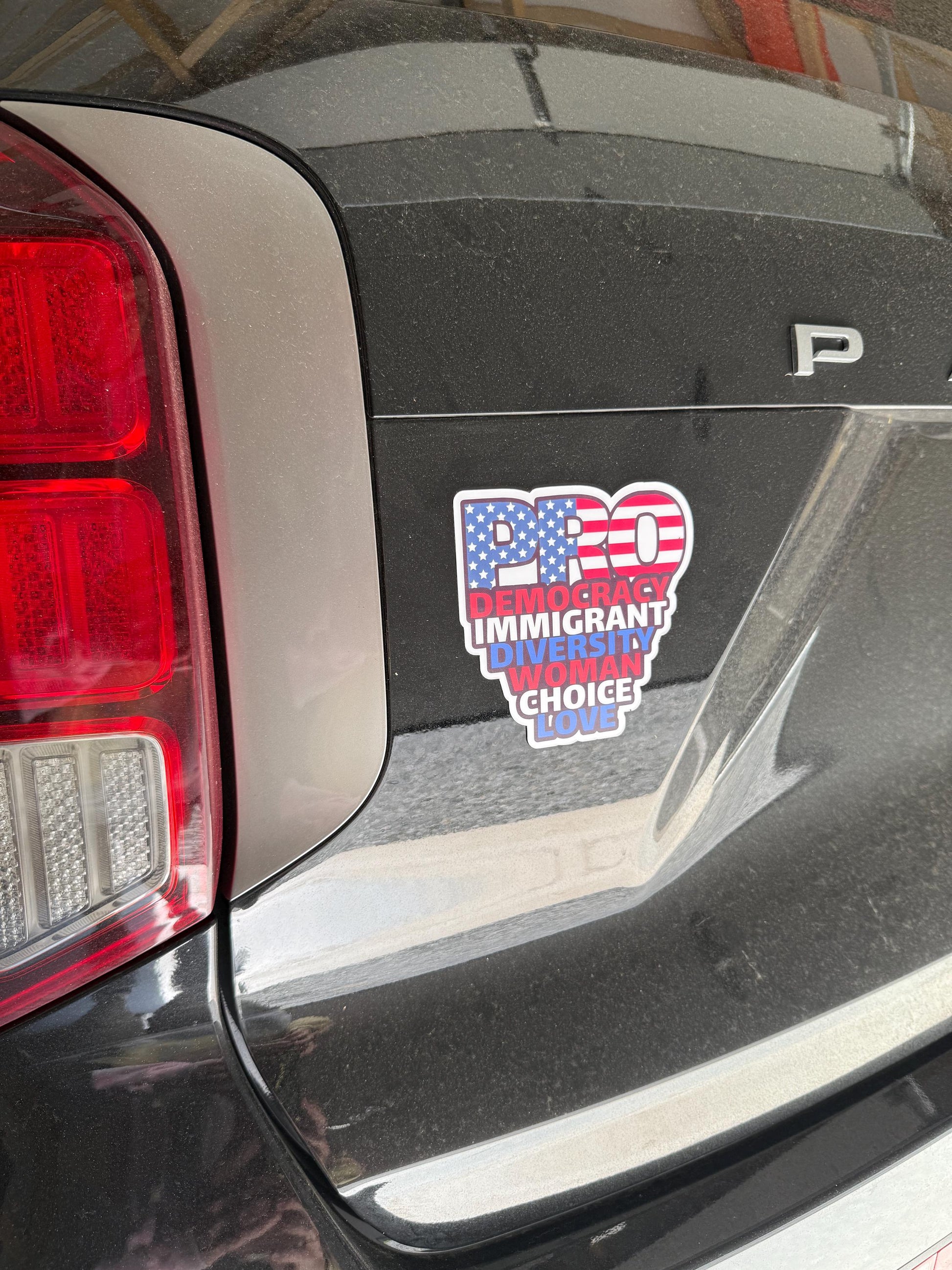 Red, white, and blue "PRO" democracy vinyl decal displayed on the back of a black SUV near the taillight.
