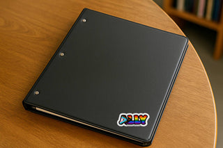 Progress pride “ALLY” sticker on a black binder resting on a wooden table
