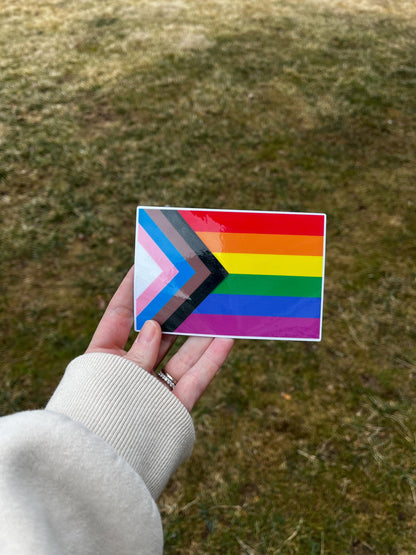 'Progressive Gay Pride Flag' magnet or vinyl decal displayed in hand. A bold, high-quality political sticker perfect for cars, laptops, fridges, or toolboxes. Great for activists, protestors, or anyone fed up with fascism.