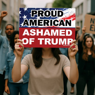 Person holding Proud American Ashamed of Trump anti-Trump protest sign at a political demonstration with protesters in the background.