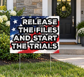Release the Files and Start the Trials outdoor political yard sign displayed on metal stakes in a residential front lawn near a home entrance. Patriotic American flag protest lawn sign calling for the release of Epstein files and government accountability.