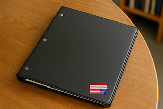 Black binder on a wooden table with a reversible American flag sticker in the lower corner.