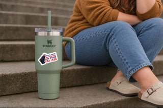 Anti-Trump political vinyl sticker on a sage green Stanley tumbler sitting on outdoor steps, featuring Donald Trump bending over and a bold red, white, and blue White House ballroom protest slogan.