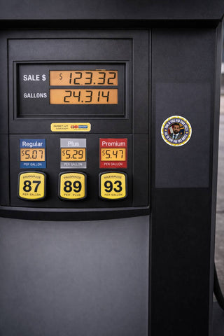 Anti-authority political satire sticker displayed on a black gas pump with bold circular protest design and irreverent slogan.