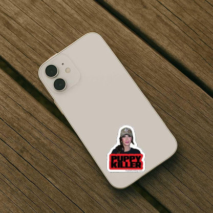 Phone case with a sticker of Kristi Noem wearing a cap and 'Puppy Killer' text on a wooden surface