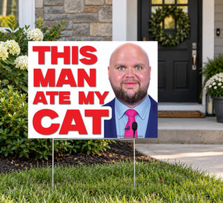This Man Ate My Cat funny political protest yard sign placed in a landscaped front lawn outside a suburban home with a black front door, featuring oversized red typography and a bald politician image.