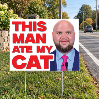Anti-MAGA political humor lawn sign reading This Man Ate My Cat in oversized red letters next to a bald politician portrait, installed in green grass along a neighborhood street.