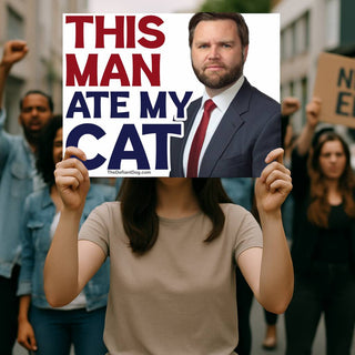 Protester holding a This Man Ate My Cat political protest sign featuring oversized red and blue text and a portrait of JD Vance, with demonstrators in the background.