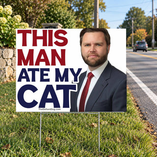Funny This Man Ate My Cat political yard sign featuring bold red and navy lettering and a portrait of a JD Vance, displayed along a suburban roadside on a metal H-stake.