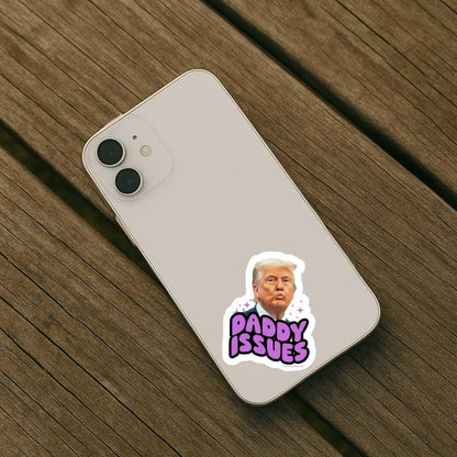 Phone with a picture of trump that says 'Daddy Issues' sticker on a wooden surface