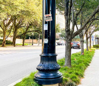 Black lamp post with stickers on a street lined with trees