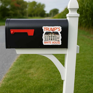 Black mailbox with a sticker of the White House and 'TRUMP'S WHITE HOUSE' text on a grassy lawn.