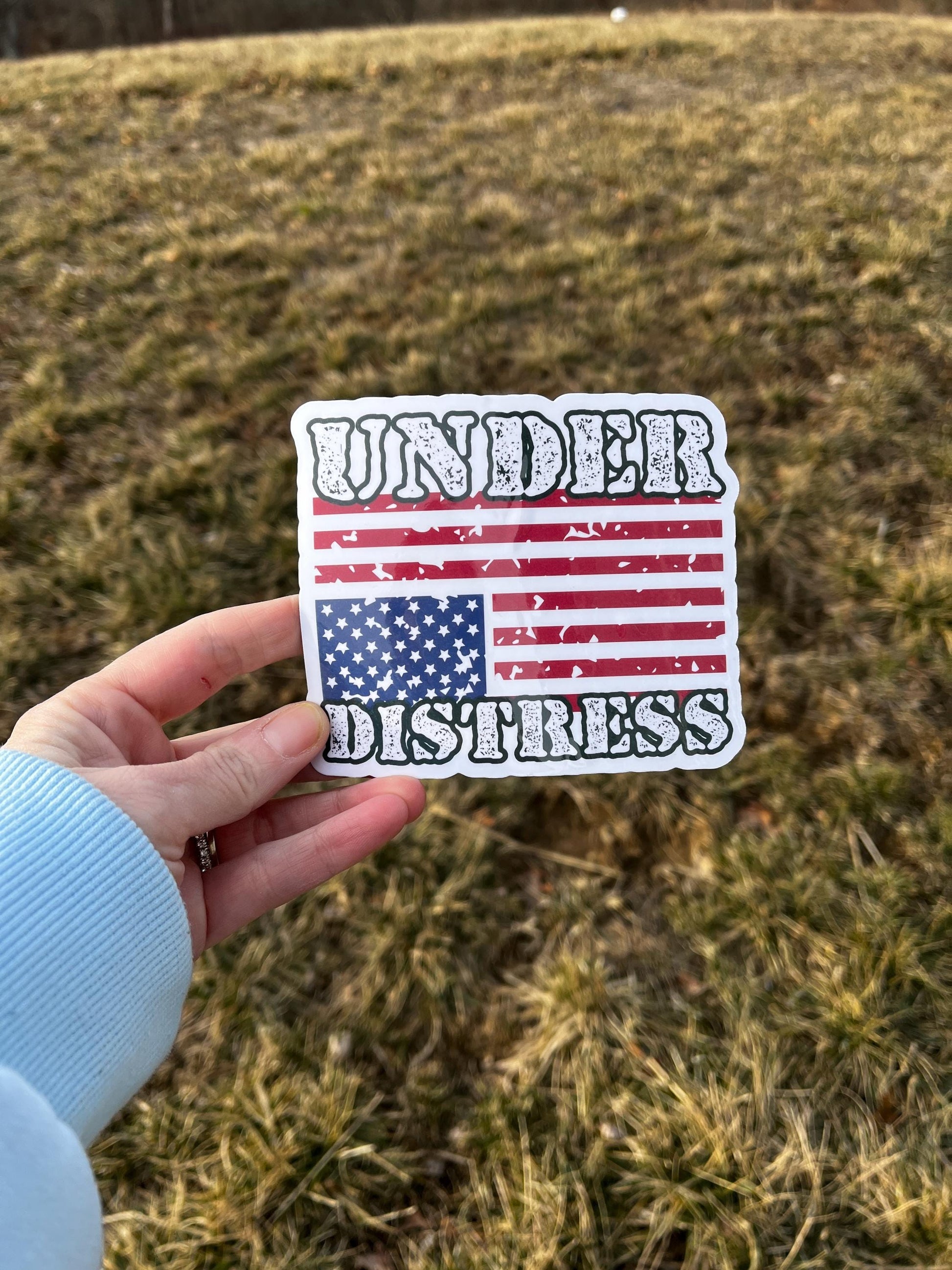 Under Distress magnet with an upside-down American flag held in hand, representing protest and urgent political resistance.