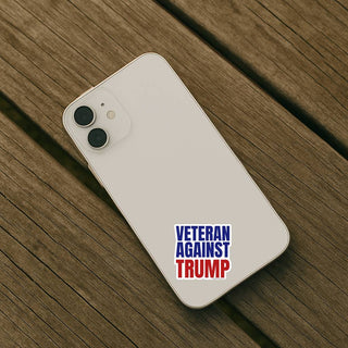 Veteran Against Trump sticker applied to the back of a light-colored smartphone resting on a wooden table.
