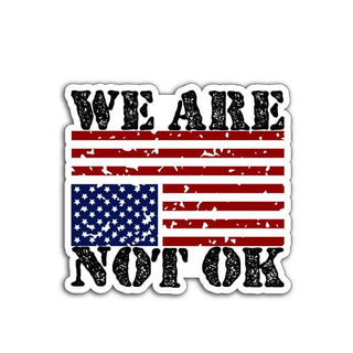 A vinyl decal or magnet featuring the phrase "We are not OK" in bold lettering, displayed alongside or over an upside-down American flag. The design symbolizes national distress and conveys a message of concern, protest, and social or political unrest.