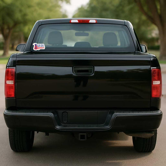 Black pickup truck with a sticker on the back window, parked on a road with trees in the background.
