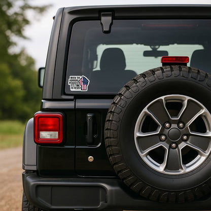 The sticker is applied to the rear window of a black Jeep Wrangler, positioned to the left of the spare tire. The background shows a blurred dirt path and trees.