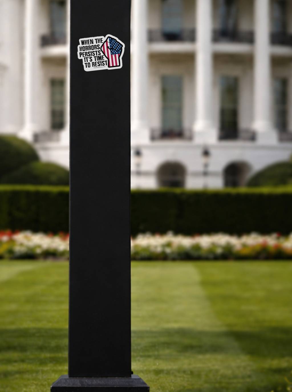 The sticker is affixed to a black square lamp post in the foreground. In the soft-focus background, the iconic architecture of the White House and its green lawn are visible.