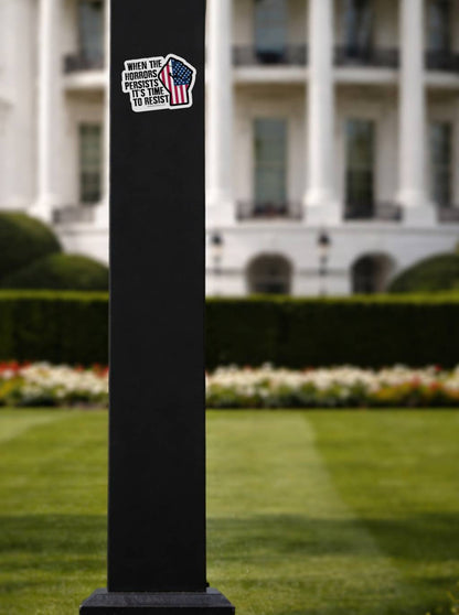 The sticker is affixed to a black square lamp post in the foreground. In the soft-focus background, the iconic architecture of the White House and its green lawn are visible.
