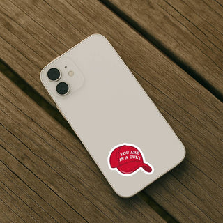 Phone case with a red cap graphic and text 'You are in a cult' on a wooden surface