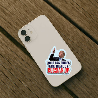 Your Gas Prices Are Really Russian Up funny political vinyl sticker displayed on the back of a white smartphone resting on a rustic wooden table.