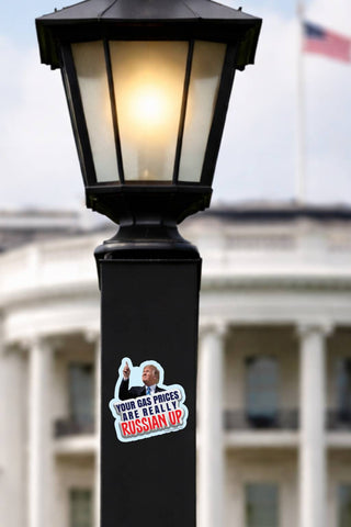 Funny Trump Russia gas prices political sticker attached to a black decorative lamppost in front of a white government-style building with an American flag.